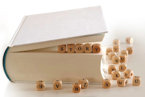 Story, message for creativ writing spelled with wooden letter blocks between pages of a white book,