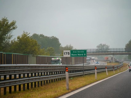 A highway scene under an overcast sky featuring cars and trucks with road signs and an overpass,