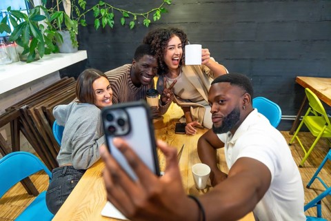 Diverse coworkers smiling taking selfie in the cafeteria of a modern coworking space