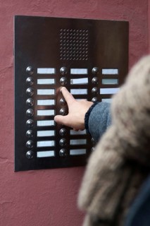 unrecognizable person ringing doorbell at apartment building. many blank nameplates