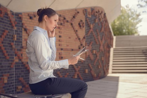 Woman doing business in a commercial foyer sitting on a wall mounted bench against patterned