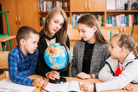 Young woman teaching geography pupil with globe