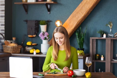 Happy female smiling and cutting cucumber for healthy vegetable salad while watching recipe on