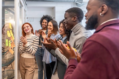 Diverse females and males mulit-ethnic colleagues applauding after a successful meeting in a modern