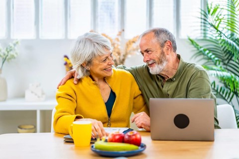 Senior couple celebrating good news on household budget sitting on the living room using laptop