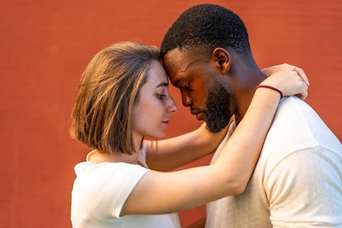 Close-up side view of multi-ethnic lovers embracing against red wall