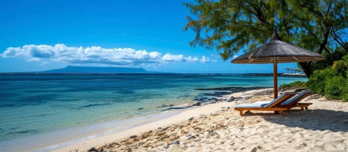 Tropical beach scene with lounge chairs under an umbrella, clear blue sky, and calm ocean waters,