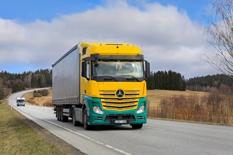 Yellow and green Mercedes-Benz Actros 1845 truck pulls curtainside semi trailer along highway on a