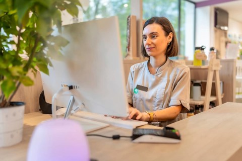 Young female pharmacist using computer sitting in the counter of a modern pharmacy store