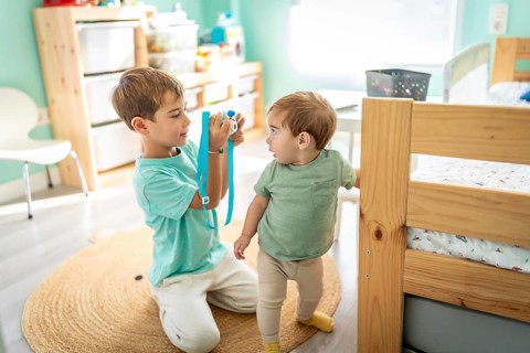 Male little photographer taking a photo of a his baby boy brother in the bedroom
