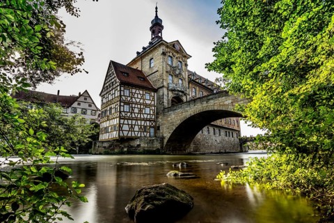 Idyllic half-timbered house on a bridge over a river surrounded by lush greenery and clouds in the