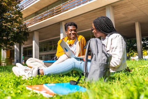 African american students studying with laptop together sitting in the grass outside the campus