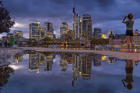 Clouds pass over the glowing Frankfurt bank skyline reflected in a puddle in the evening, Mainufer,