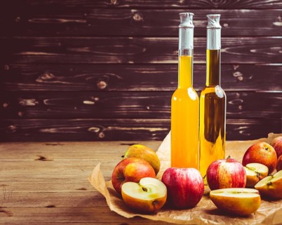 Apple juice with apple vinegar in bottles and fresh apples on wooden background