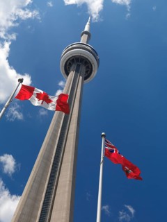 Ontario and Canada flags flying in front of Toronto CN tower over blue sky