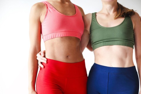 Two joyful happy women in sportive pink hoodie taking break after yoga classes or workout, standing