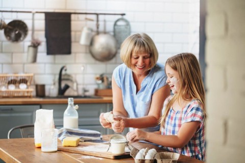 Happy adult mature woman cooking together with cute little girl at table in kitchen