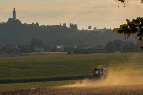 Typical Bavarian rural farm labor scene with tractor plowing field and pilgrimage church on top of