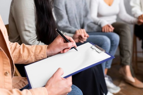 Man writing clipboard group therapy session