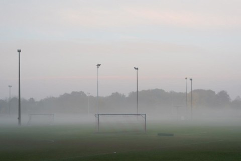 Empty and deserted soccer field in suburban area with goals and flood light poles on grey overcast