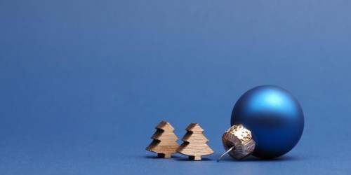 Blue Christmas tree ball with small wooden tree shapes on a blue paper background with space for