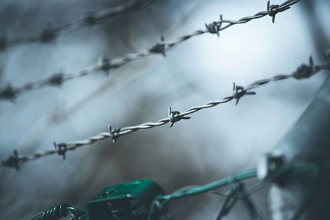 Barbed wire on a metal fence to demarcate the border, closeup, blurry background