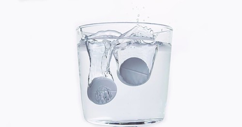 Tablets Falling and Dissolving into a Glass of Water against White Background