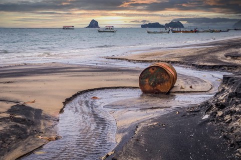 Rusty barrel oil on a partly black coloured beach illustrates the pollution of environment by oil
