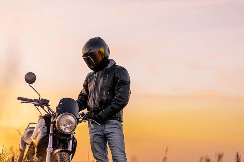Motorcyclist in a helmet and motorcycle clothing stands at an old cafe racer