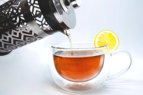 Glass teapot pouring black tea into cup isolated on the white