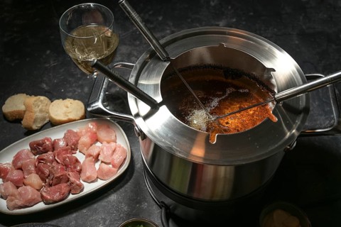 Fondue pot with boiling hot oil, long forks and raw meat, party dinner for friends and family,