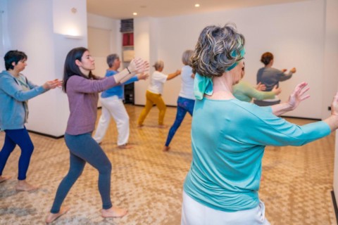 Group of women simulating waves in a choreographed Qi Gong exercise in a classroom