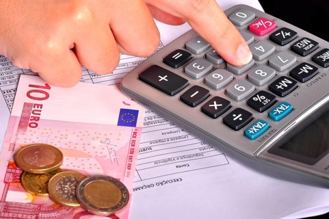 Business person doing accounts using a calculator with some money on the side