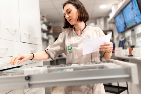 Young female pharmacist searching medicines in the drawer of storage room