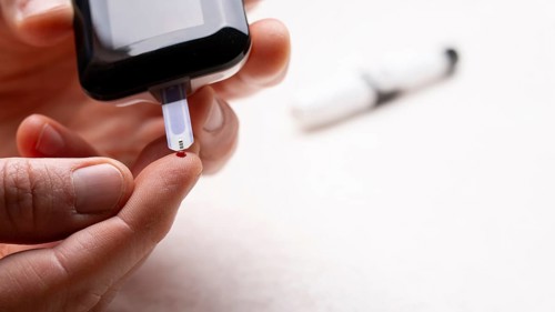 Pierced caucasian finger ready to measure glucose level by glucose meter closeup view with