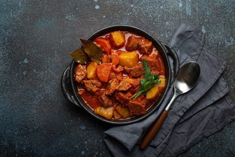 Beef meat stew with potatoes, carrot and delicious gravy in black casserole pot with bay leaves and