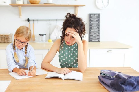 ?ute school girl wearing eyeglasses doing homework with mother at home on the kitchen