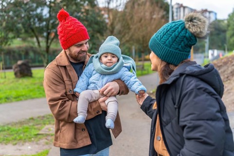Parents holding their baby while enjoying a winter day outdoors in a park, wearing warm clothes and