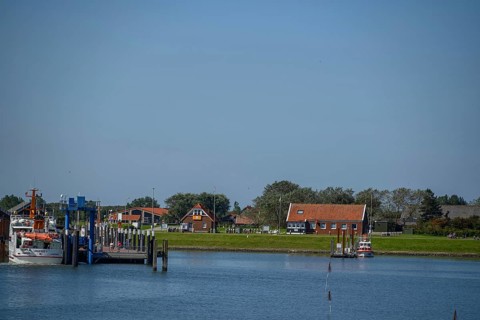 Small boats and traditional buildings at the harbour with calm water and blue sky, langeoog, east
