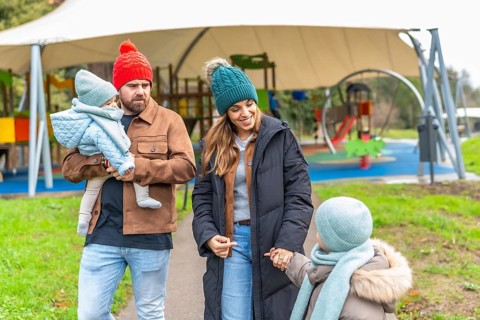 Happy family enjoying a winter day at the playground, bundled up in warm clothes and colorful hats,