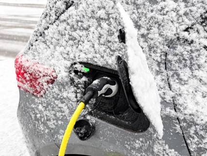 Charging an electric vehicle in winter. A yellow charging cable is connected to the car's charging