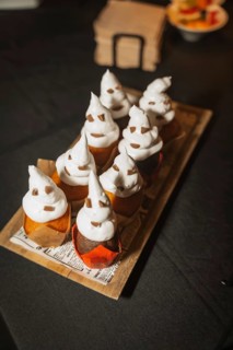 Halloween food and sweets in the shape of pumpkins at a party, chocolate ghost cupcakes