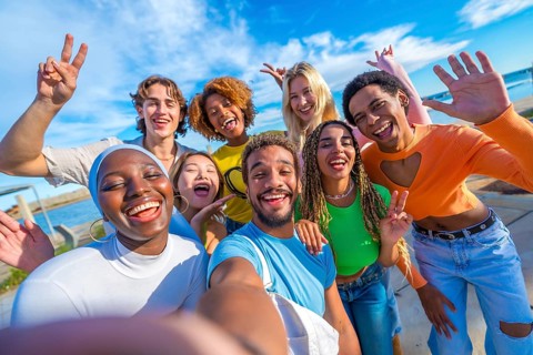 Happy multiracial friends taking a selfie and gesturing outdoors