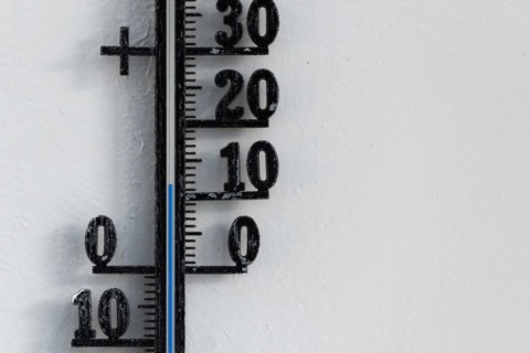 Classic analog thermometer hanging on white wall displaying warmth of twelve degrees celsius
