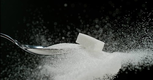 White Sugar Cube falling on Powder Sugar against Black Background