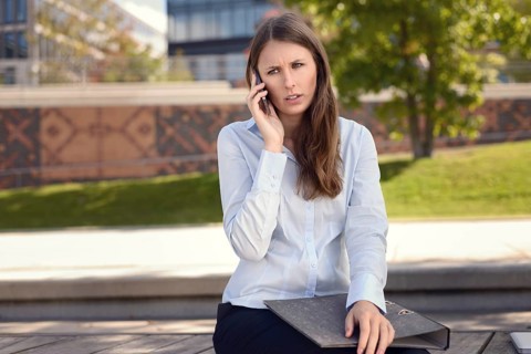 Irritated young woman frowning in annoyance as she sits outdoors in the shade of a tree in an urban