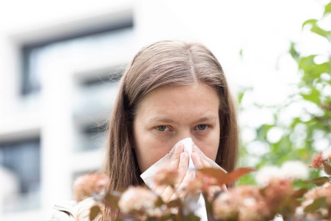 Young woman suffers from hay fever and uses a paper handkerchief outdoors, Freiburg,