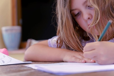 Close-up of a beautiful blonde girl in a colorful dress concentrating on school homework
