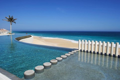 Modern infinity pool overlooking a sandy beach and the ocean under a clear blue sky, in the coast