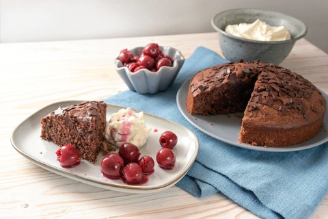 Homemade chocolate cake with morello cherries and whipped cream on a blue napkin and a bright